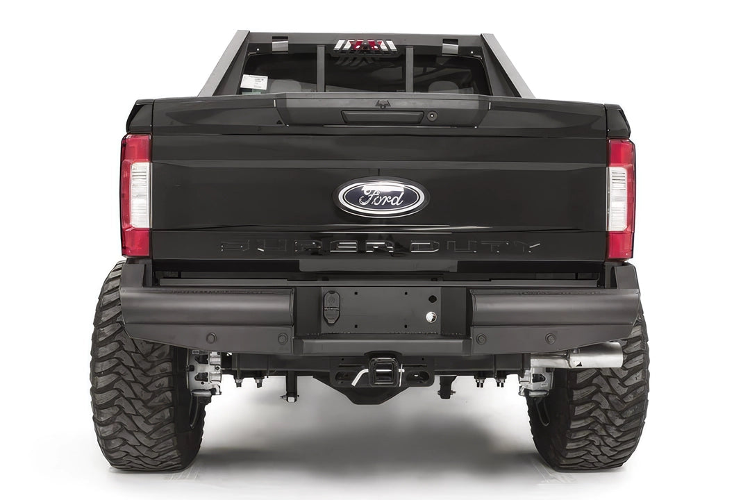 Fab Fours Black Steel Elite rear bumper on a black Ford Super Duty, straight-on rear view, showing the smooth steel face, the center license plate recess, and the receiver hitch access