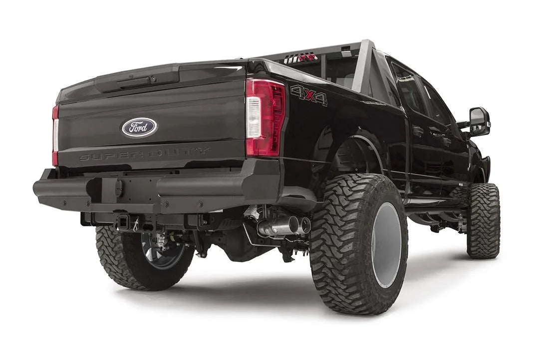 Fab Fours Black Steel Elite rear bumper on a black Ford Super Duty, rear passenger-side three-quarter view, showing the smooth steel face, the center license plate recess, and the receiver hitch access
