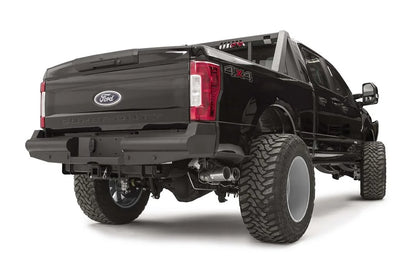 Fab Fours Black Steel Elite rear bumper on a black Ford Super Duty, rear passenger-side three-quarter view, showing the smooth steel face, the center license plate recess, and the receiver hitch access