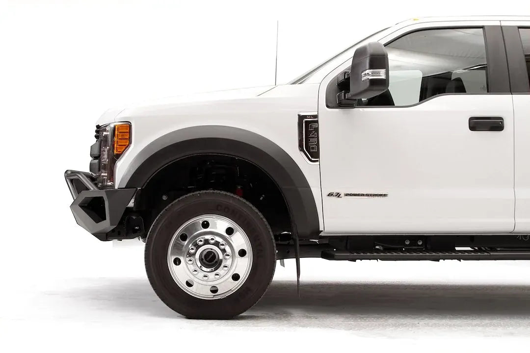 Fab Fours Vengeance front bumper with pre-runner guard on a white Ford Super Duty F-450/F-550, driver-side profile view of the front corner, showing the tubular pre-runner hoop, the center LED light bar, cube light pods, and the open skid plate design