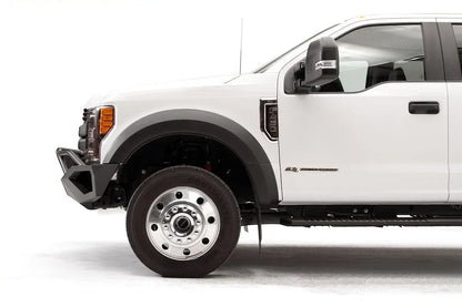 Fab Fours Vengeance front bumper with pre-runner guard on a white Ford Super Duty F-450/F-550, driver-side profile view of the front corner, showing the tubular pre-runner hoop, the center LED light bar, cube light pods, and the open skid plate design