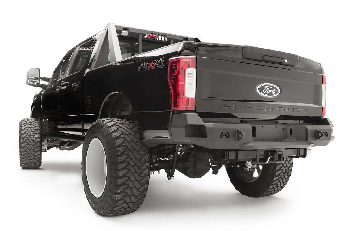 Fab Fours Premium rear bumper on a black Ford Super Duty, rear driver-side three-quarter view, showing the center license plate recess, integrated light openings, and angular steel end caps