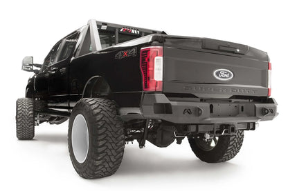 Fab Fours Premium rear bumper on a black Ford Super Duty, rear driver-side three-quarter view, showing the center license plate recess, integrated light openings, and angular steel end caps