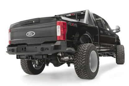 Fab Fours Premium rear bumper on a black Ford Super Duty, rear passenger-side three-quarter view, showing the center license plate recess, integrated light openings, and angular steel end caps