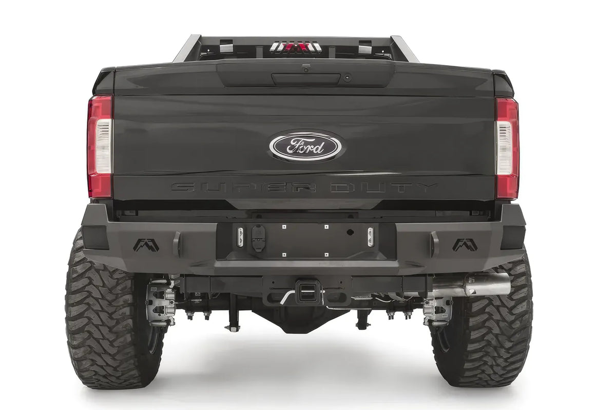 Fab Fours Premium rear bumper on a black Ford Super Duty, straight-on rear view, showing the center license plate recess, integrated light openings, and angular steel end caps