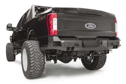Fab Fours Premium rear bumper on a black Ford Super Duty, rear driver-side three-quarter view, showing the center license plate recess, integrated light openings, and angular steel end caps
