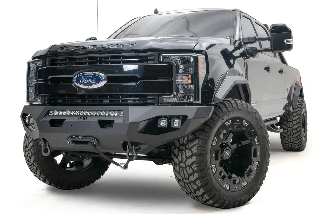 Fab Fours Matrix front bumper on a black Ford Super Duty F-250/F-350, front driver-side three-quarter view, showing the center LED light bar, cube light pods, and the integrated winch with shackle mounts