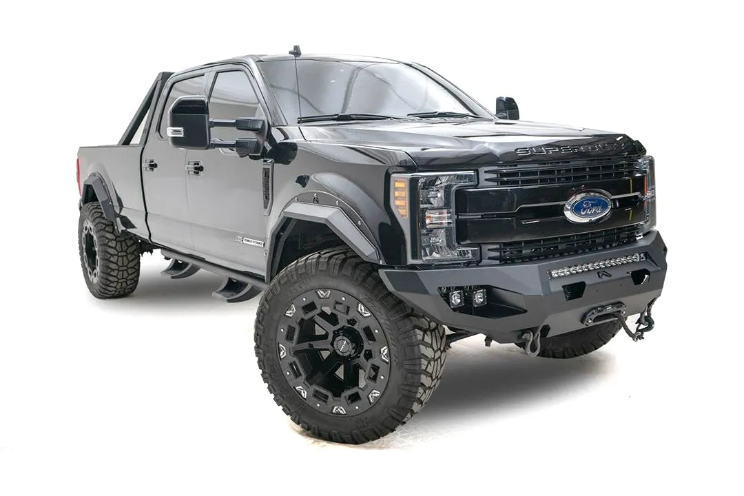 Fab Fours Matrix front bumper on a black Ford Super Duty F-250/F-350, front passenger-side three-quarter view, showing the center LED light bar, cube light pods, and the integrated winch with shackle mounts