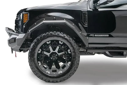 Fab Fours Matrix front bumper with pre-runner guard on a black Ford Super Duty F-250/F-350, driver-side profile view of the front corner, showing the tubular pre-runner hoop, the center LED light bar, cube light pods, and the integrated winch with shackle mounts