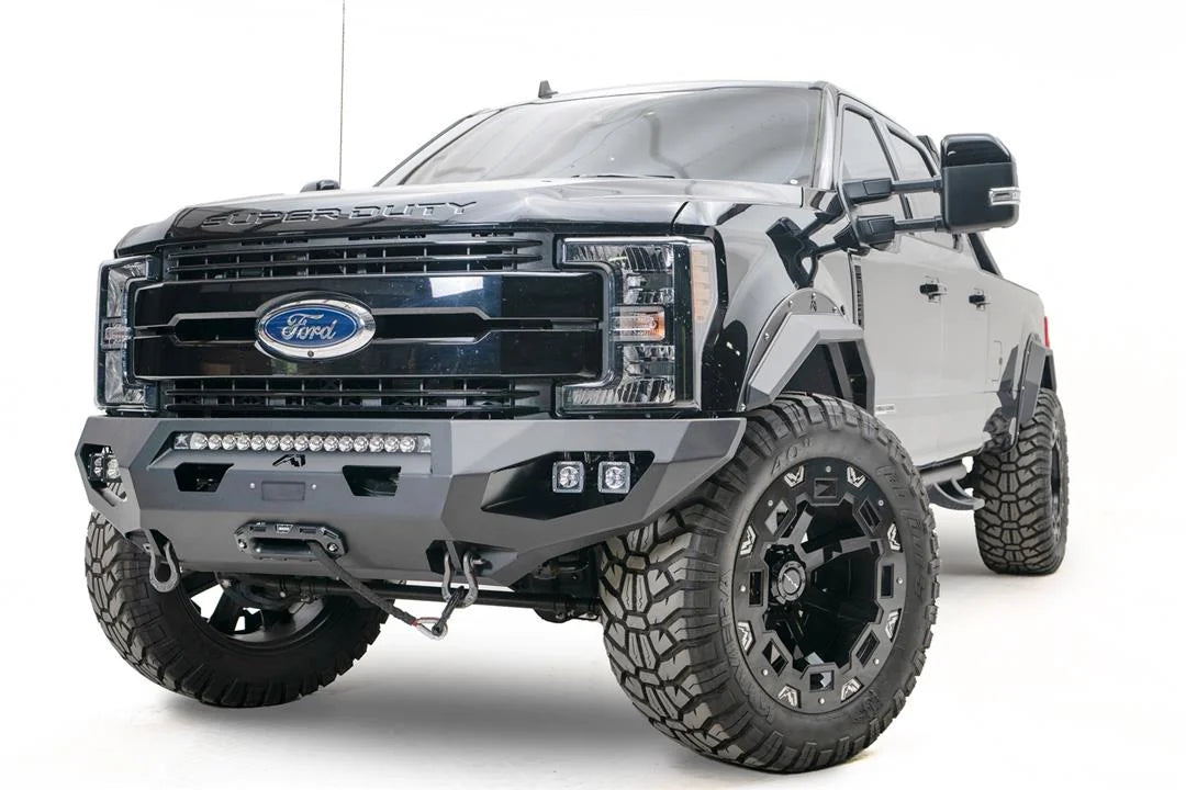 Fab Fours Matrix front bumper on a black Ford Super Duty F-250/F-350, front driver-side three-quarter view, showing the center LED light bar, cube light pods, and the integrated winch with shackle mounts