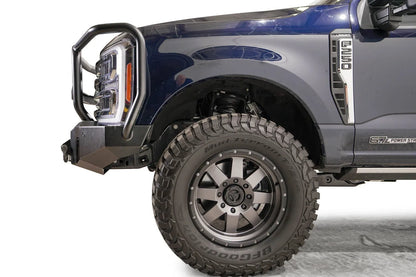 Fab Fours Premium Winch front bumper with full guard on a dark blue Ford Super Duty F-250/F-350, driver-side profile view of the front corner, showing full grille guard hoops, the center winch plate with fairlead, LED light pods, and D-ring shackle mounts
