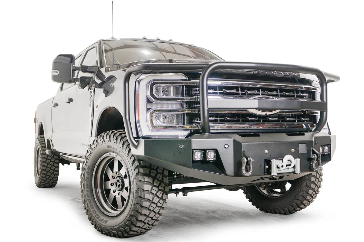 Fab Fours Premium Winch front bumper with full guard on a blue and gray two-tone Ford Super Duty F-250/F-350, front passenger-side three-quarter view, showing full grille guard hoops, the center winch plate with fairlead, LED light pods, and D-ring shackle mounts