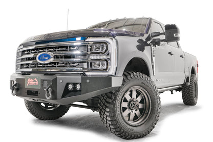 Fab Fours Premium Winch front bumper on a blue and gray two-tone Ford Super Duty F-250/F-350, front driver-side three-quarter view, showing the center winch plate with fairlead, LED light pods, and D-ring shackle mounts