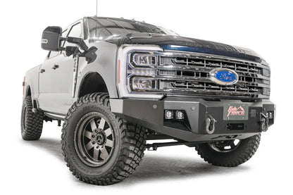Fab Fours Premium Winch front bumper on a blue and gray two-tone Ford Super Duty F-250/F-350, front passenger-side three-quarter view, showing the center winch plate with fairlead, LED light pods, and D-ring shackle mounts