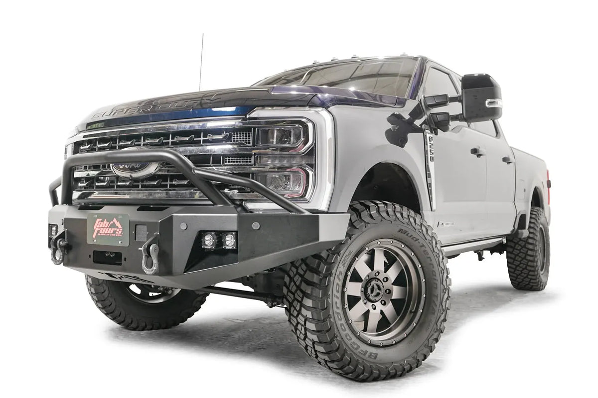 Fab Fours Premium Winch front bumper with pre-runner guard on a blue and gray two-tone Ford Super Duty F-250/F-350, front driver-side three-quarter view, showing the tubular pre-runner hoop, the center winch plate with fairlead, LED light pods, and D-ring shackle mounts