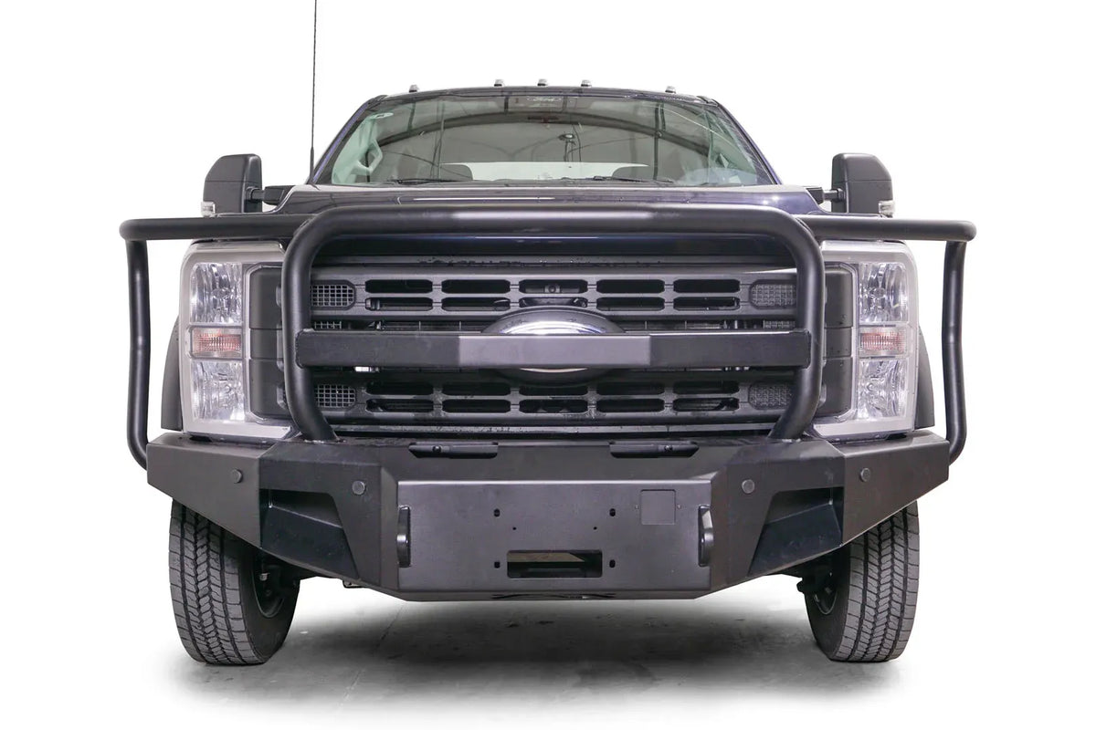 Fab Fours Premium Winch front bumper with full guard on a blue and gray two-tone Ford Super Duty F-450/F-550, straight-on front view, showing full grille guard hoops, the center winch plate, angular end caps, and recessed light openings