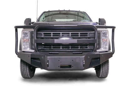 Fab Fours Premium Winch front bumper with full guard on a blue and gray two-tone Ford Super Duty F-450/F-550, straight-on front view, showing full grille guard hoops, the center winch plate, angular end caps, and recessed light openings