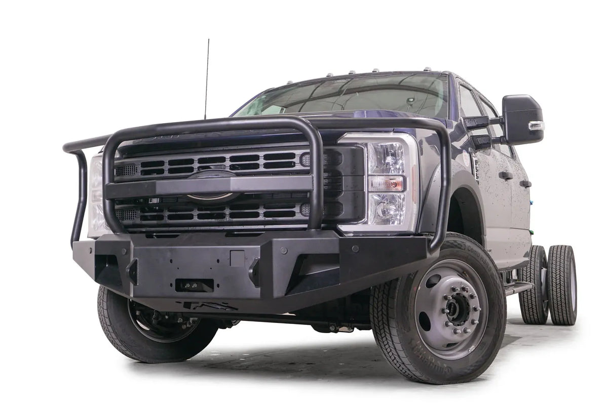 Fab Fours Premium Winch front bumper with full guard on a blue and gray two-tone Ford Super Duty F-450/F-550, front driver-side three-quarter view, showing full grille guard hoops, the center winch plate, angular end caps, and recessed light openings