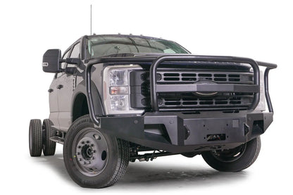 Fab Fours Premium Winch front bumper with full guard on a blue and gray two-tone Ford Super Duty F-450/F-550, front passenger-side three-quarter view, showing full grille guard hoops, the center winch plate, angular end caps, and recessed light openings
