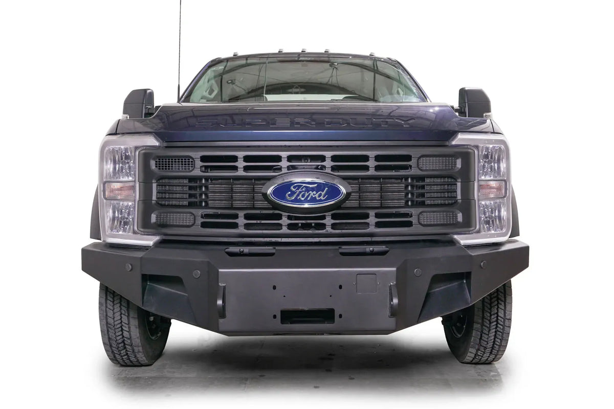 Fab Fours Premium Winch front bumper on a dark blue Ford Super Duty F-450/F-550, straight-on front view, showing the center winch plate, angular end caps, and recessed light openings