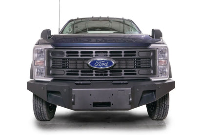 Fab Fours Premium Winch front bumper on a dark blue Ford Super Duty F-450/F-550, straight-on front view, showing the center winch plate, angular end caps, and recessed light openings