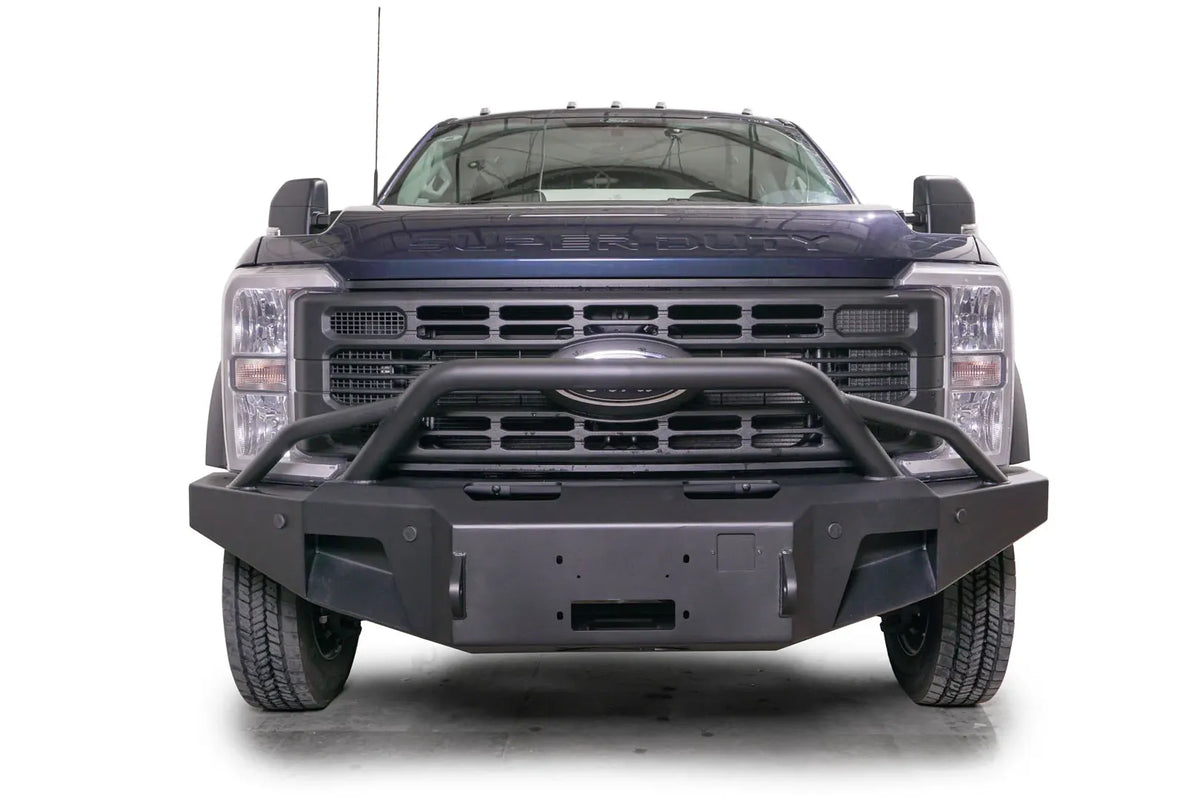 Fab Fours Premium Winch front bumper with pre-runner guard on a blue and gray two-tone Ford Super Duty F-450/F-550, straight-on front view, showing the tubular pre-runner hoop, the center winch plate, angular end caps, and recessed light openings