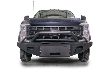 Fab Fours Premium Winch front bumper with pre-runner guard on a blue and gray two-tone Ford Super Duty F-450/F-550, straight-on front view, showing the tubular pre-runner hoop, the center winch plate, angular end caps, and recessed light openings