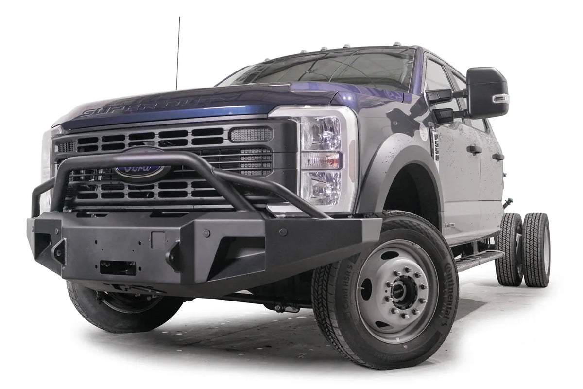 Fab Fours Premium Winch front bumper with pre-runner guard on a blue and gray two-tone Ford Super Duty F-450/F-550, front driver-side three-quarter view, showing the tubular pre-runner hoop, the center winch plate, angular end caps, and recessed light openings