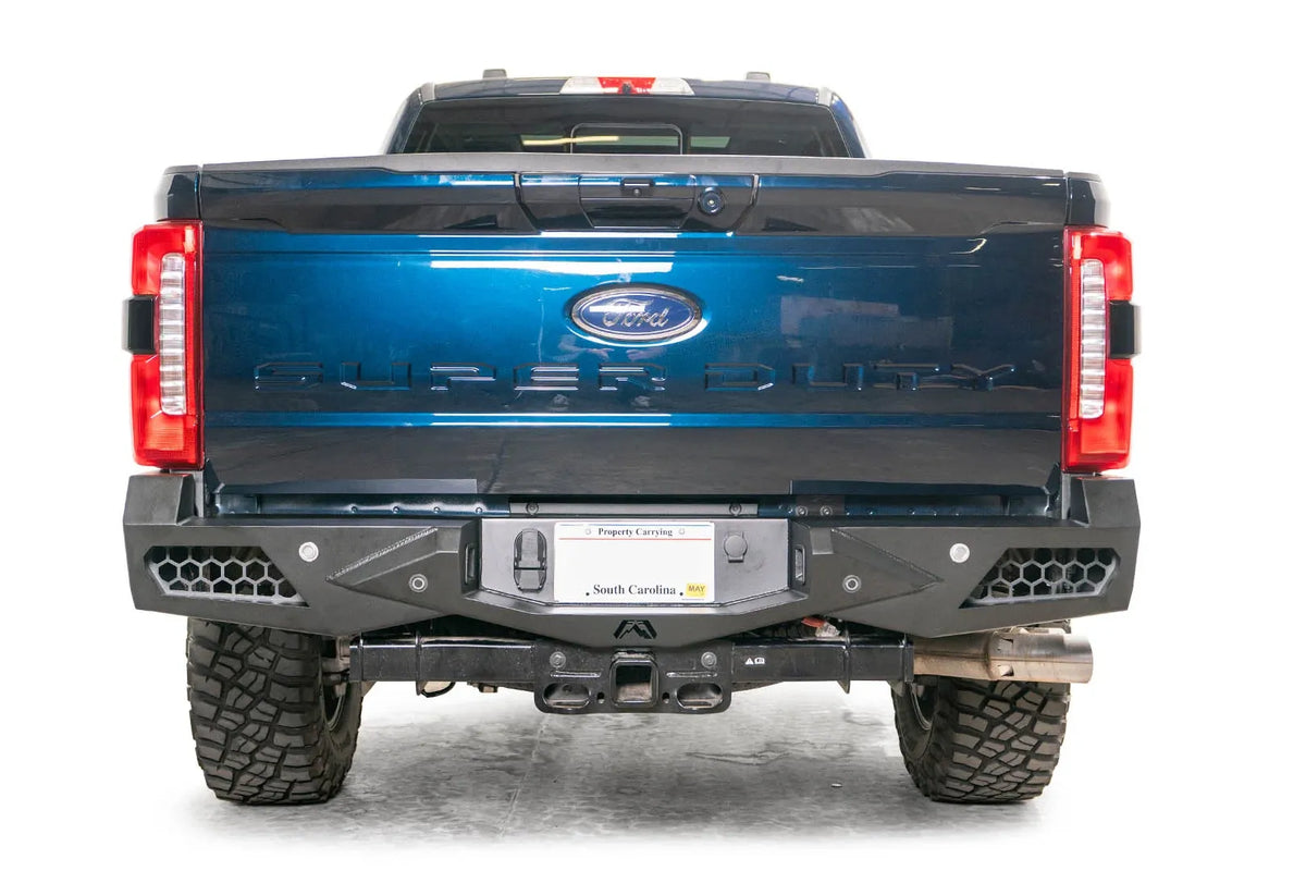 Fab Fours Vengeance rear bumper on a blue Ford Super Duty, straight-on rear view, showing honeycomb-pattern side cutouts, the center license plate recess, and the receiver hitch access