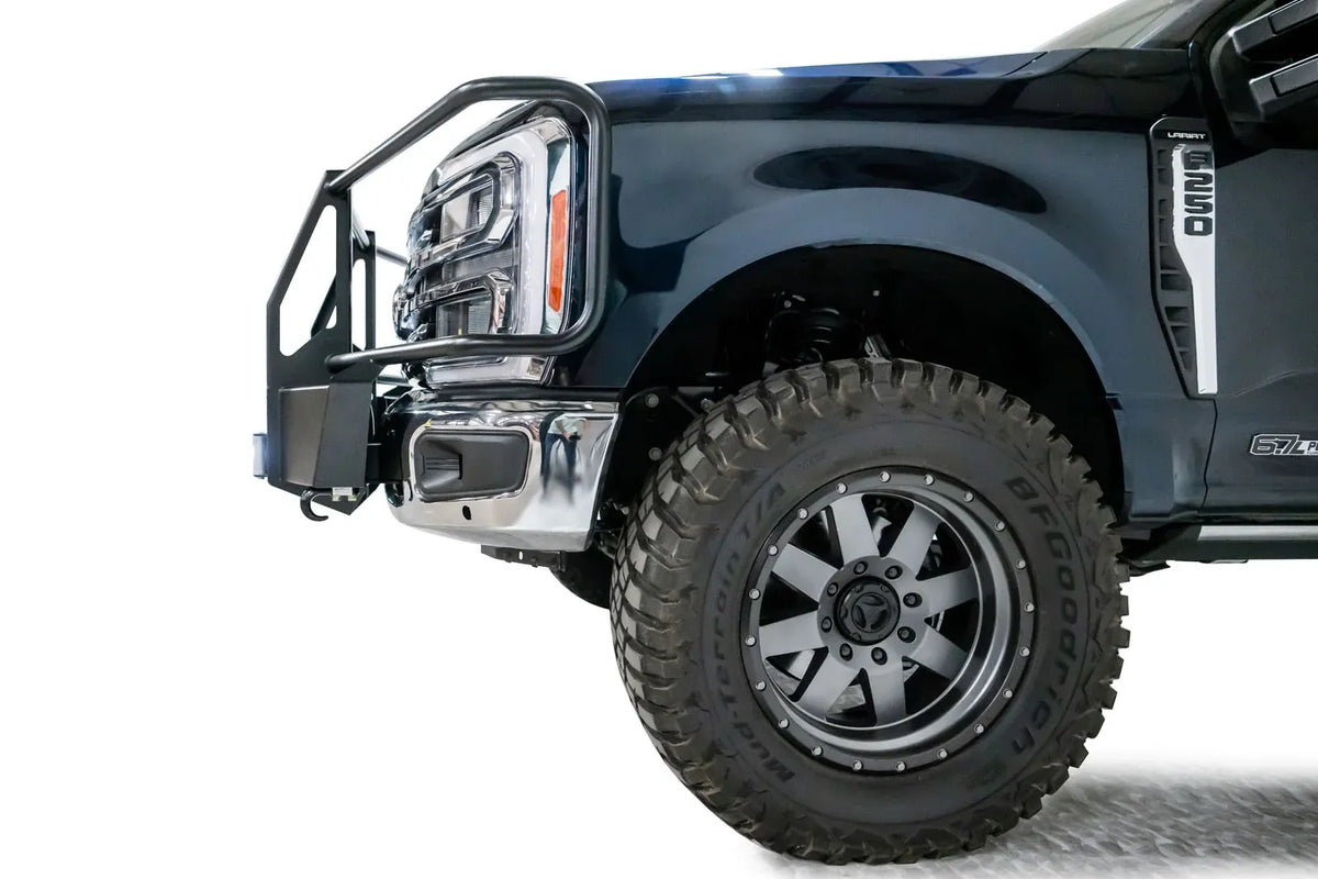 Fab Fours winch mount with full guard on a dark blue Ford Super Duty F-250/F-350, driver-side profile view of the front corner, showing full grille guard uprights and hoops, the winch mount plate with fairlead and the factory bumper integration