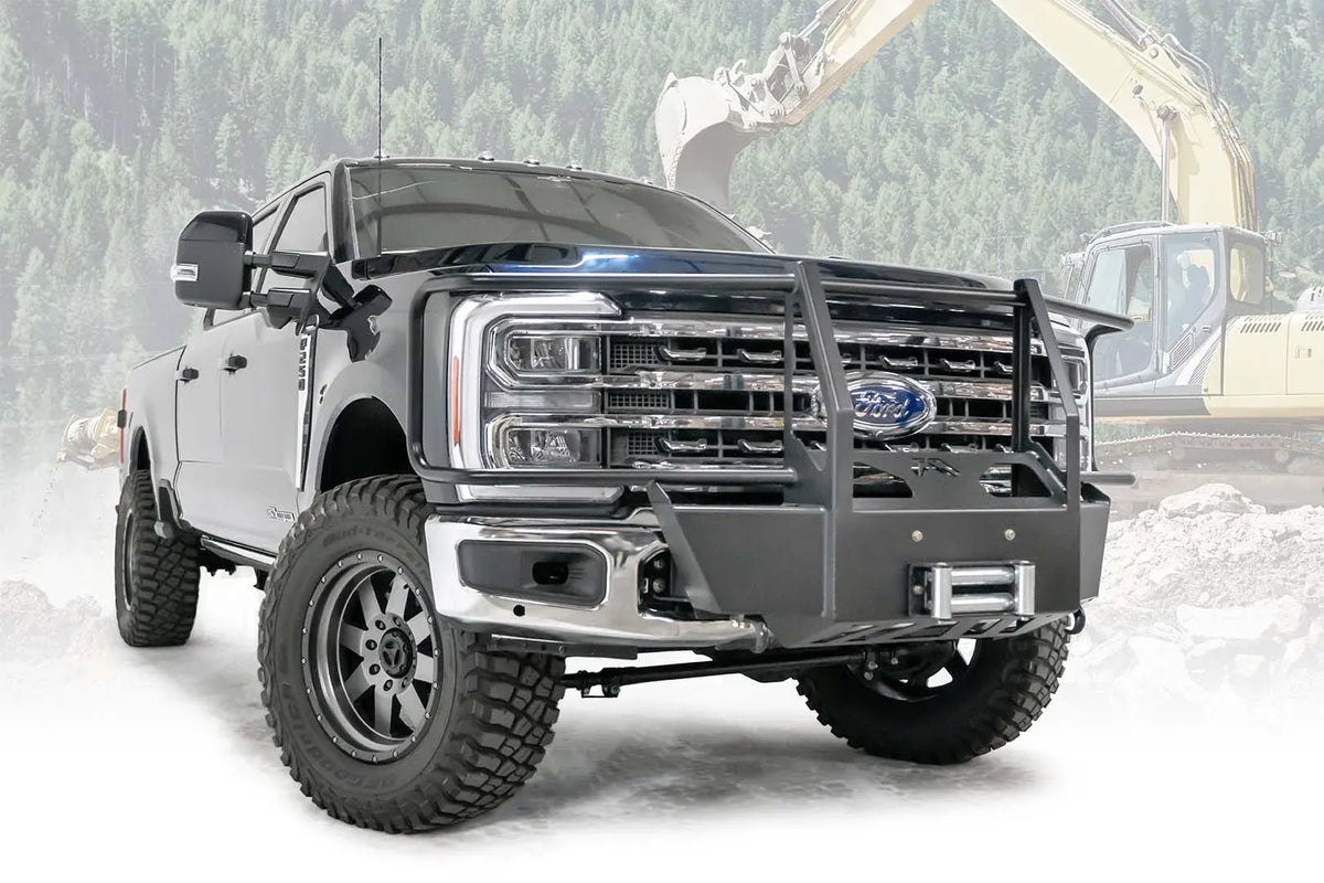 Fab Fours winch mount with full guard on a blue and gray two-tone Ford Super Duty F-250/F-350, front passenger-side three-quarter view outdoors, showing full grille guard uprights and hoops, the winch mount plate with fairlead and the factory bumper integration
