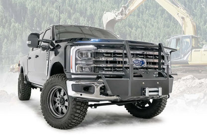 Fab Fours winch mount with full guard on a blue and gray two-tone Ford Super Duty F-250/F-350, front passenger-side three-quarter view outdoors, showing full grille guard uprights and hoops, the winch mount plate with fairlead and the factory bumper integration