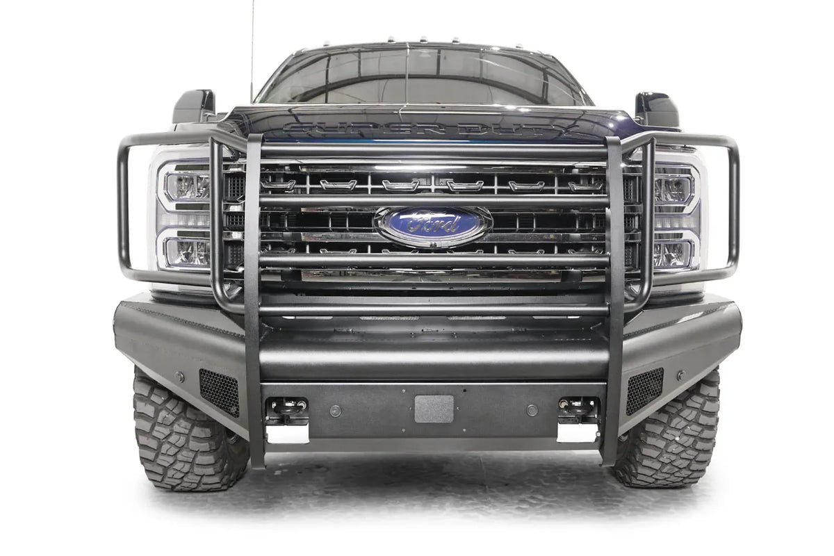 Fab Fours Black Steel Elite front bumper with full guard on a blue and gray two-tone Ford Super Duty, straight-on front view, showing full grille guard uprights and side hoops, the smooth steel face, mesh-backed side openings, and the center sensor/plate mount
