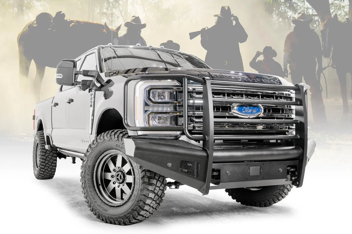 Fab Fours Black Steel Elite front bumper with full guard on a blue and gray two-tone Ford Super Duty, front passenger-side three-quarter view outdoors, showing full grille guard uprights and side hoops, the smooth steel face, mesh-backed side openings, and the center sensor/plate mount