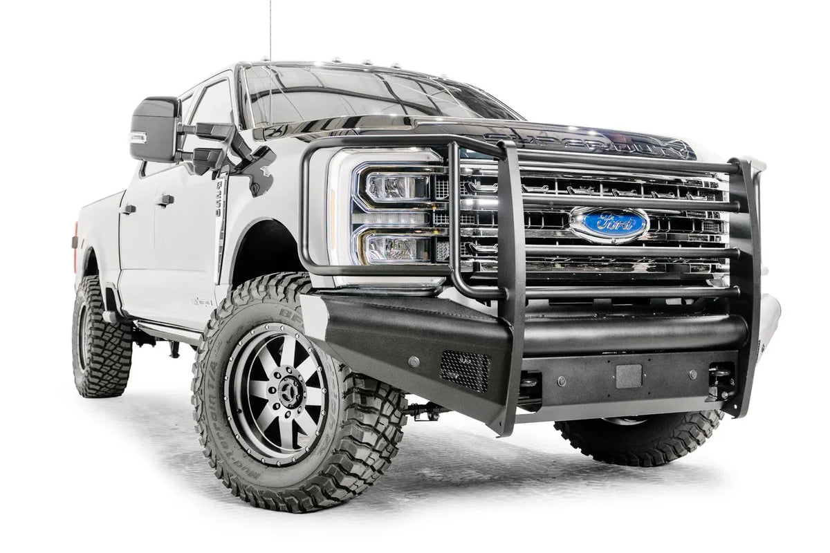 Fab Fours Black Steel Elite front bumper with full guard on a blue and gray two-tone Ford Super Duty, front passenger-side three-quarter view, showing full grille guard uprights and side hoops, the smooth steel face, mesh-backed side openings, and the center sensor/plate mount