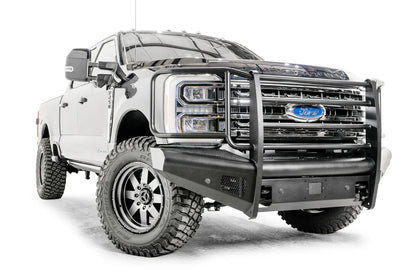 Fab Fours Black Steel Elite front bumper with full guard on a blue and gray two-tone Ford Super Duty, front passenger-side three-quarter view, showing full grille guard uprights and side hoops, the smooth steel face, mesh-backed side openings, and the center sensor/plate mount