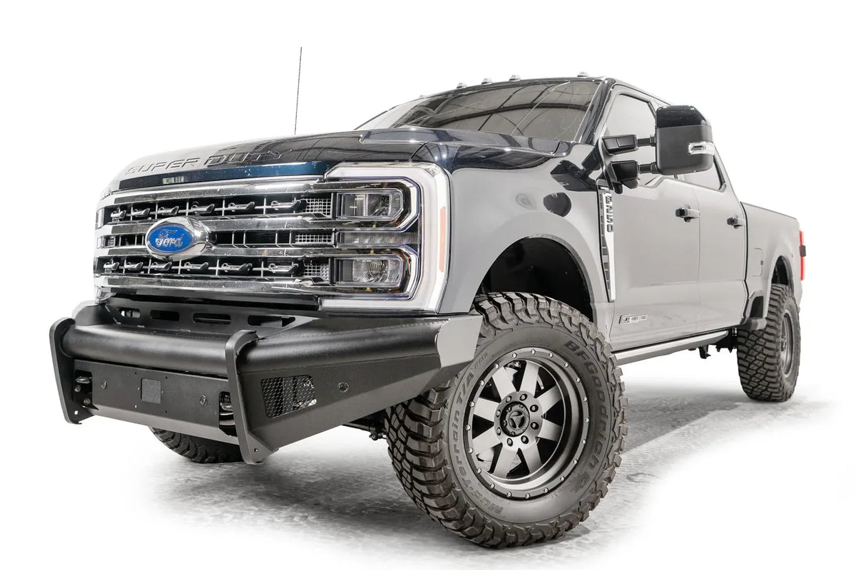 Fab Fours Black Steel Elite front bumper on a blue and gray two-tone Ford Super Duty, front driver-side three-quarter view, showing the smooth steel face, mesh-backed side openings, and the center sensor/plate mount