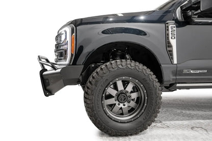 Fab Fours Black Steel Elite front bumper with pre-runner guard on a dark blue Ford Super Duty, driver-side profile view of the front corner, showing the tubular pre-runner hoop, the smooth steel face, mesh-backed side openings, and the center sensor/plate mount