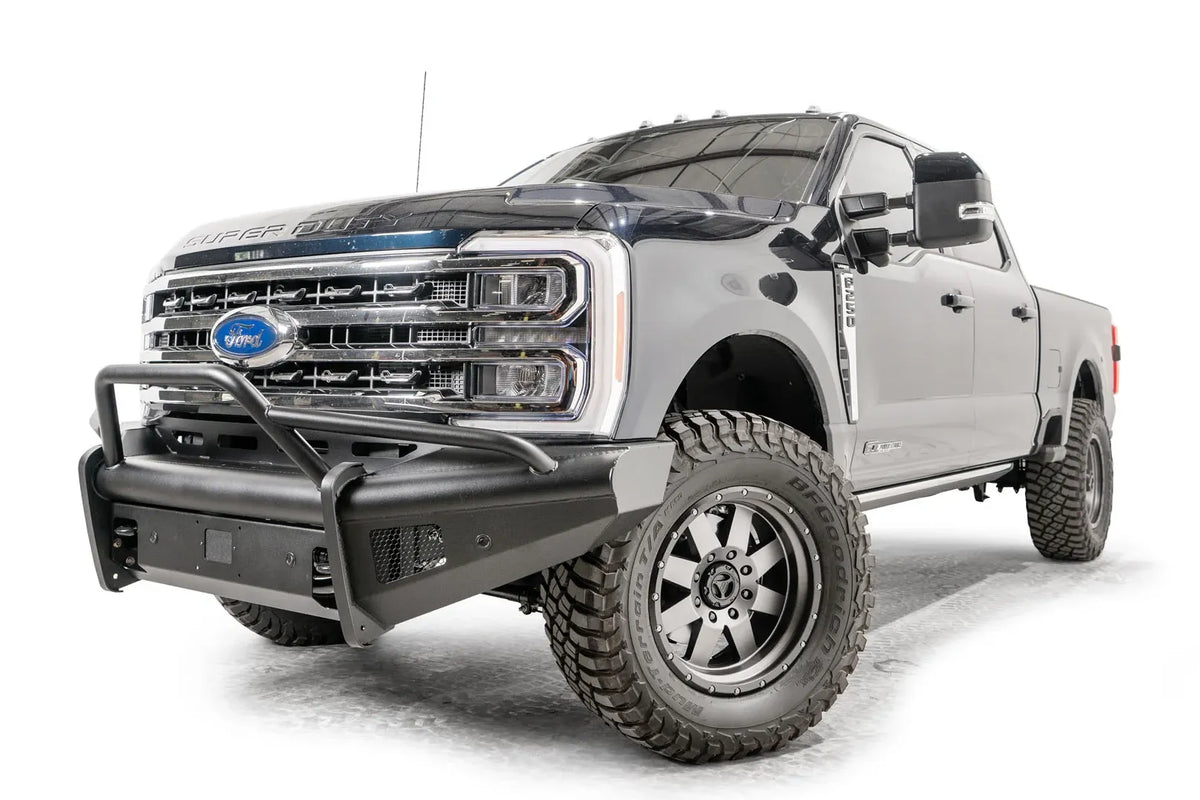 Fab Fours Black Steel Elite front bumper with pre-runner guard on a blue and gray two-tone Ford Super Duty, front driver-side three-quarter view, showing the tubular pre-runner hoop, the smooth steel face, mesh-backed side openings, and the center sensor/plate mount