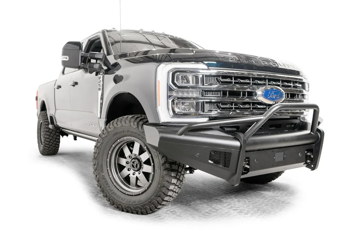 Fab Fours Black Steel Elite front bumper with pre-runner guard on a blue and gray two-tone Ford Super Duty, front passenger-side three-quarter view, showing the tubular pre-runner hoop, the smooth steel face, mesh-backed side openings, and the center sensor/plate mount
