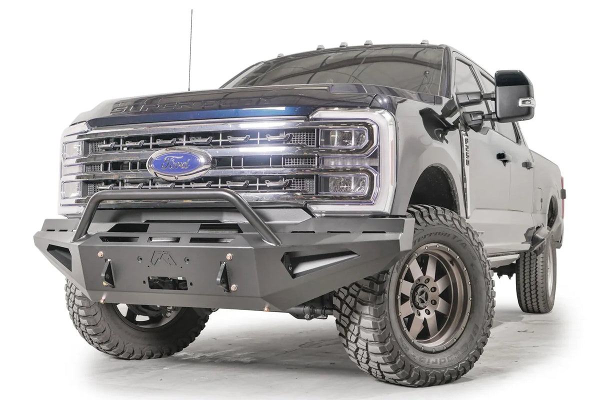 Fab Fours Red Steel front bumper with pre-runner guard on a blue and gray two-tone Ford Super Duty, front driver-side three-quarter view, showing the tubular pre-runner hoop, the center winch mount plate, and angular steel wings