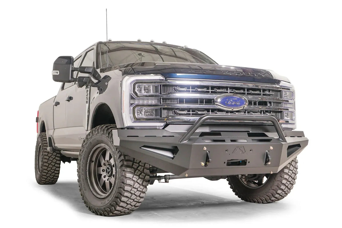 Fab Fours Red Steel front bumper with pre-runner guard on a blue and gray two-tone Ford Super Duty, front passenger-side three-quarter view, showing the tubular pre-runner hoop, the center winch mount plate, and angular steel wings