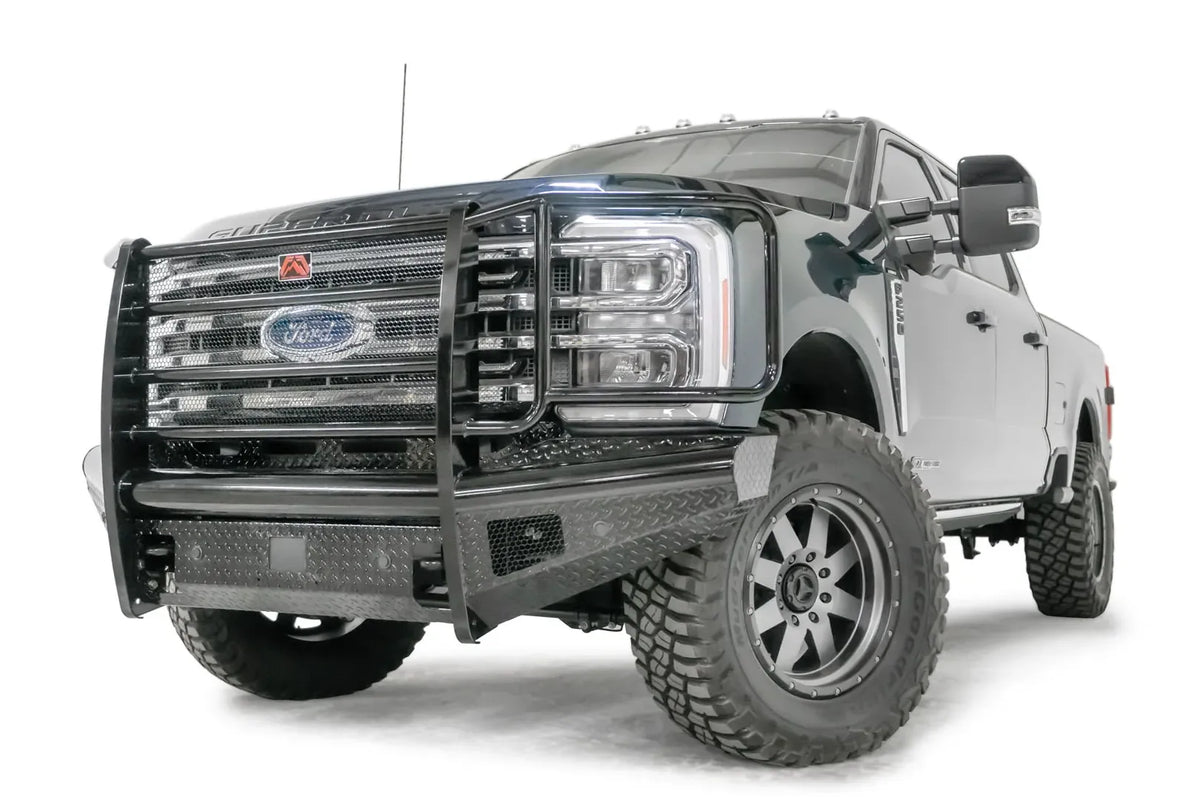 Fab Fours Black Steel front bumper with full guard on a blue and gray two-tone Ford Super Duty, front driver-side three-quarter view, showing full grille guard with mesh insert, diamond-plate face panels, the center sensor/plate mount, and angled side wings