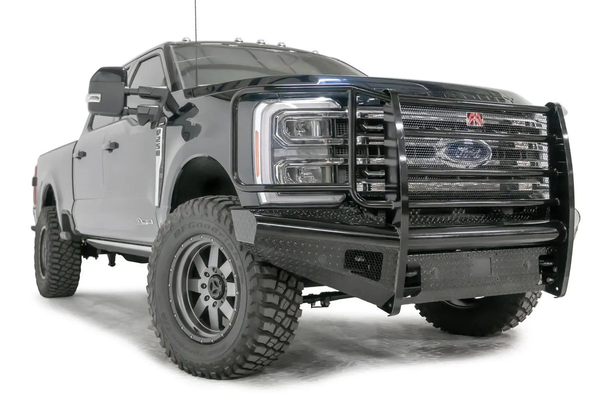 Fab Fours Black Steel front bumper with full guard on a blue and gray two-tone Ford Super Duty, front passenger-side three-quarter view, showing full grille guard with mesh insert, diamond-plate face panels, the center sensor/plate mount, and angled side wings