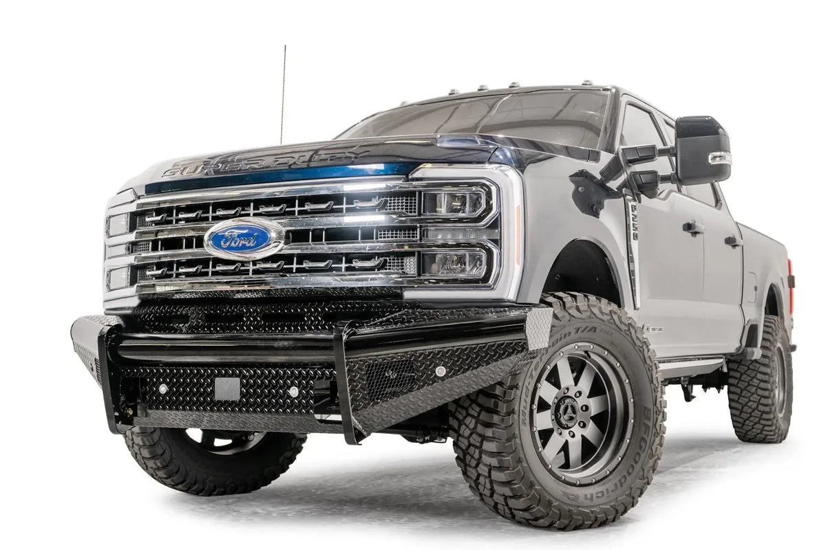 Fab Fours Black Steel front bumper on a blue and gray two-tone Ford Super Duty, front driver-side three-quarter view, showing diamond-plate face panels, the center sensor/plate mount, and angled side wings