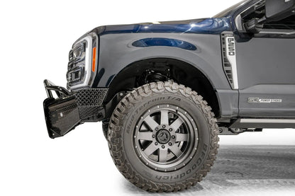 Fab Fours Black Steel front bumper with pre-runner guard on a dark blue Ford Super Duty, driver-side profile view of the front corner, showing the tubular pre-runner hoop, diamond-plate face panels, the center sensor/plate mount, and angled side wings