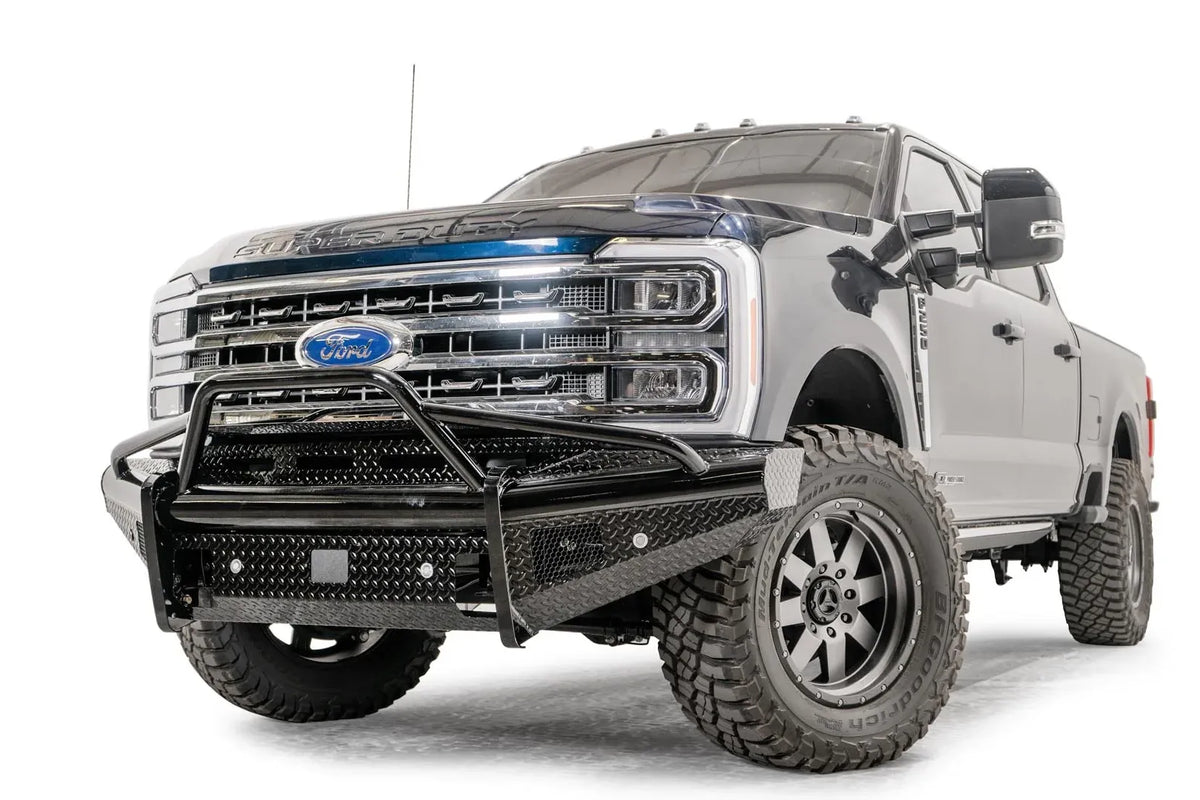 Fab Fours Black Steel front bumper with pre-runner guard on a blue and gray two-tone Ford Super Duty, front driver-side three-quarter view, showing the tubular pre-runner hoop, diamond-plate face panels, the center sensor/plate mount, and angled side wings