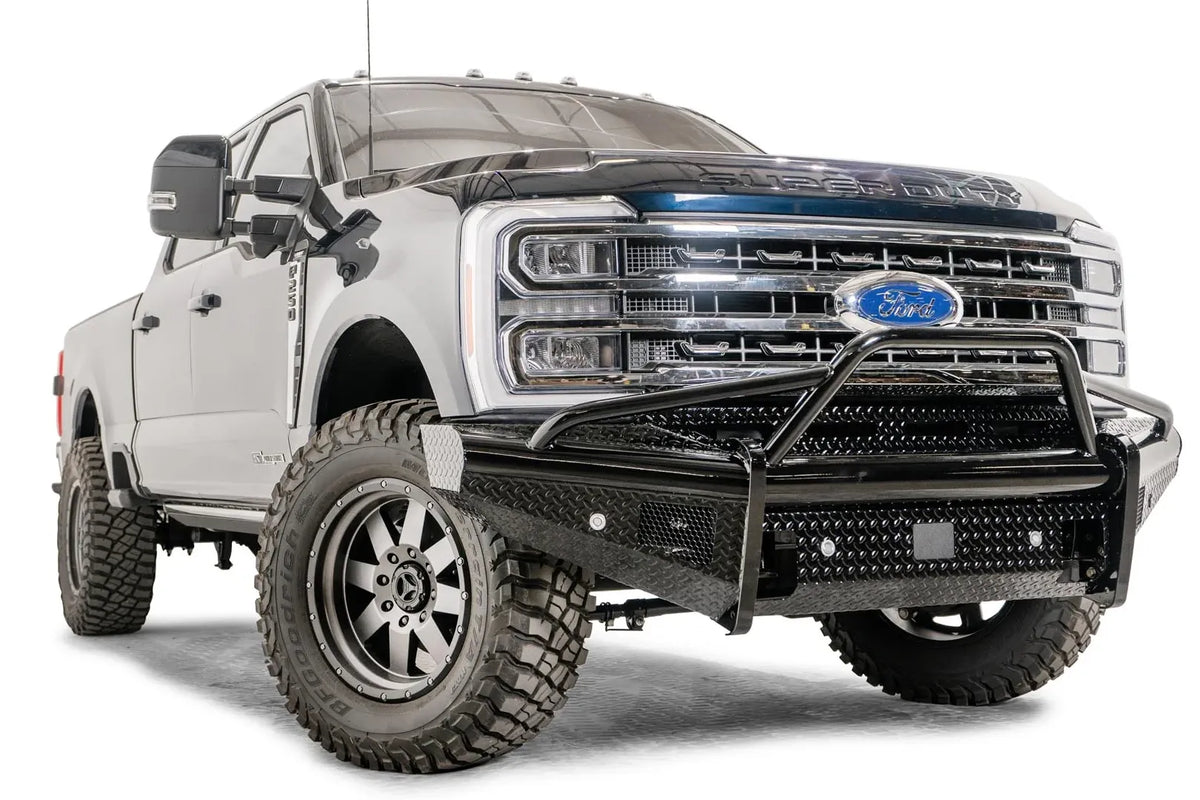 Fab Fours Black Steel front bumper with pre-runner guard on a blue and gray two-tone Ford Super Duty, front passenger-side three-quarter view, showing the tubular pre-runner hoop, diamond-plate face panels, the center sensor/plate mount, and angled side wings