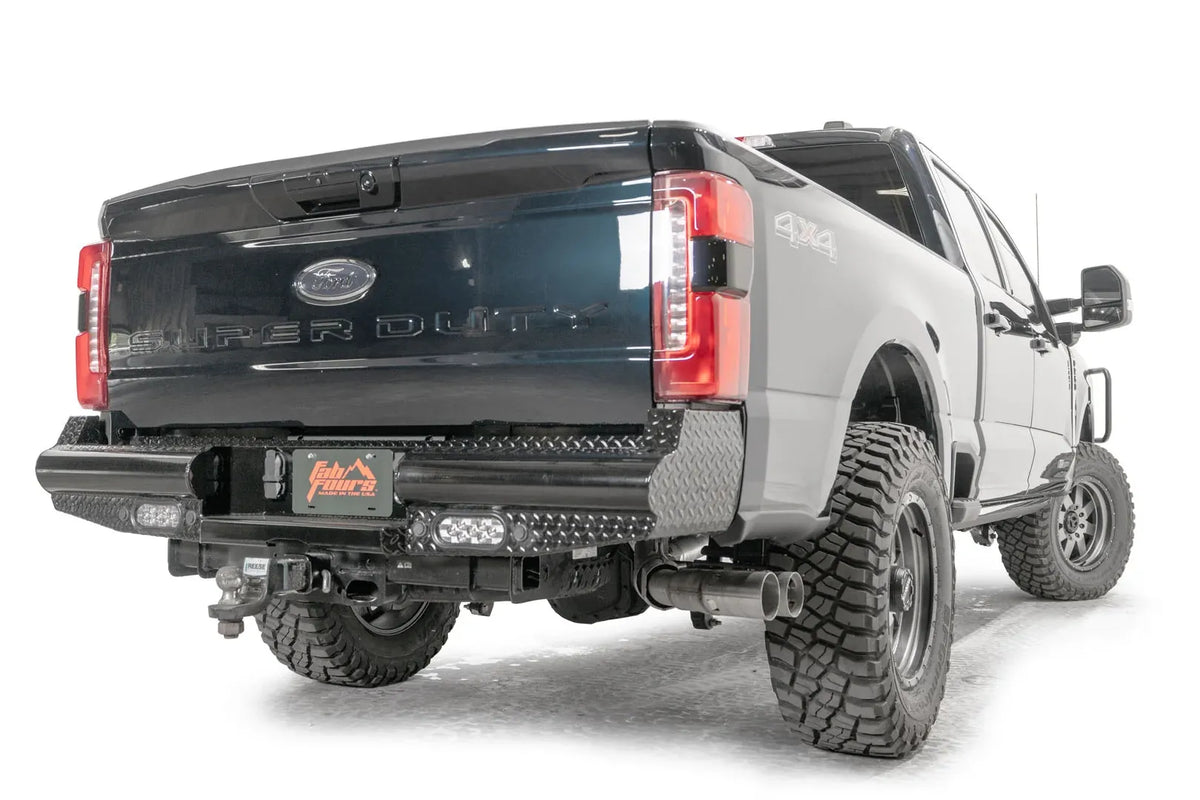 Fab Fours Black Steel rear bumper on a gray and dark blue two-tone Ford Super Duty, rear passenger-side three-quarter view, showing the diamond-plate wrap-around corners, LED lights and hitch access