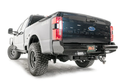 Fab Fours Black Steel rear bumper on a gray and dark blue two-tone Ford Super Duty, rear driver-side three-quarter view, showing the diamond-plate end caps, flush-mount LED lights and receiver hitch opening